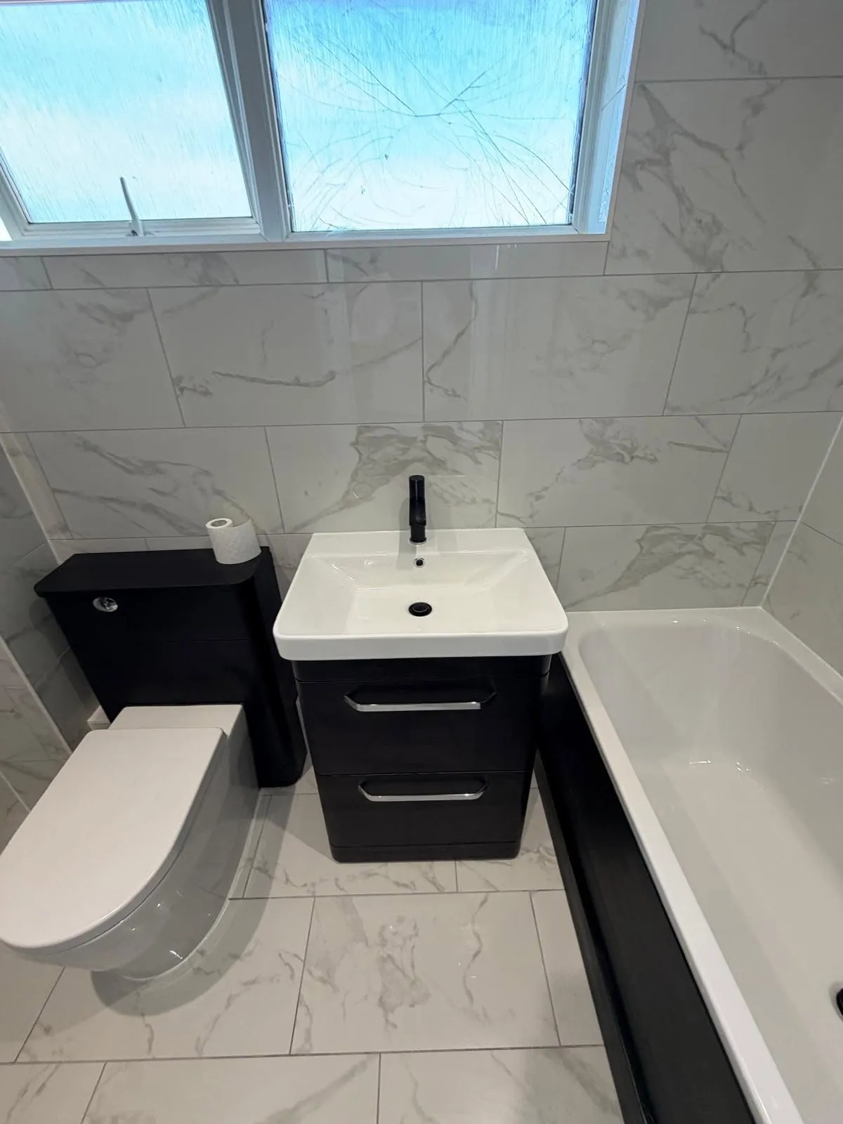 Bathroom installation by Space B Tiling: dark vanity and toilet with marble-effect wall and floor tiles