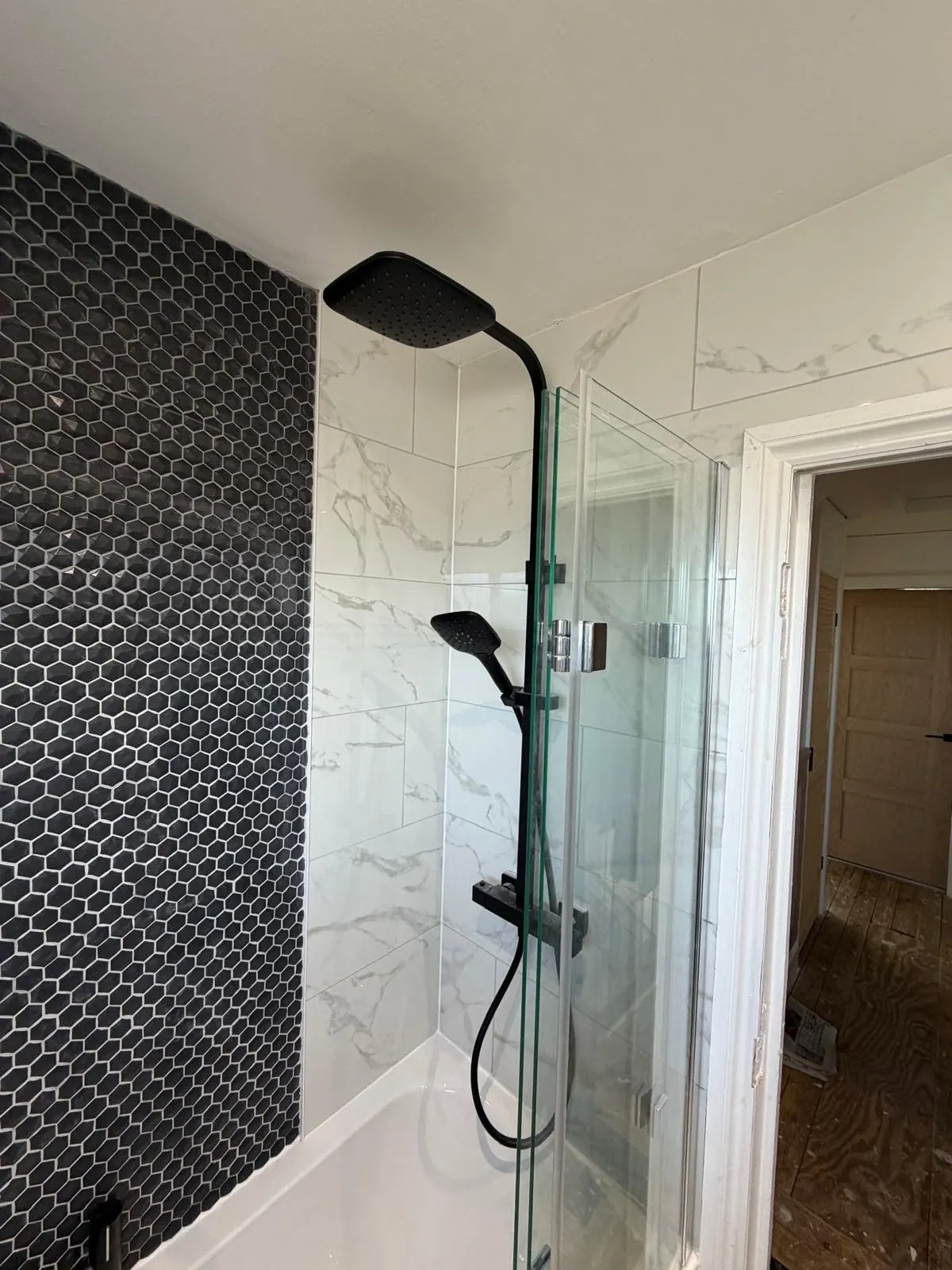 Bathroom installation by Space B Tiling: black shower set beside hexagon mosaic feature wall