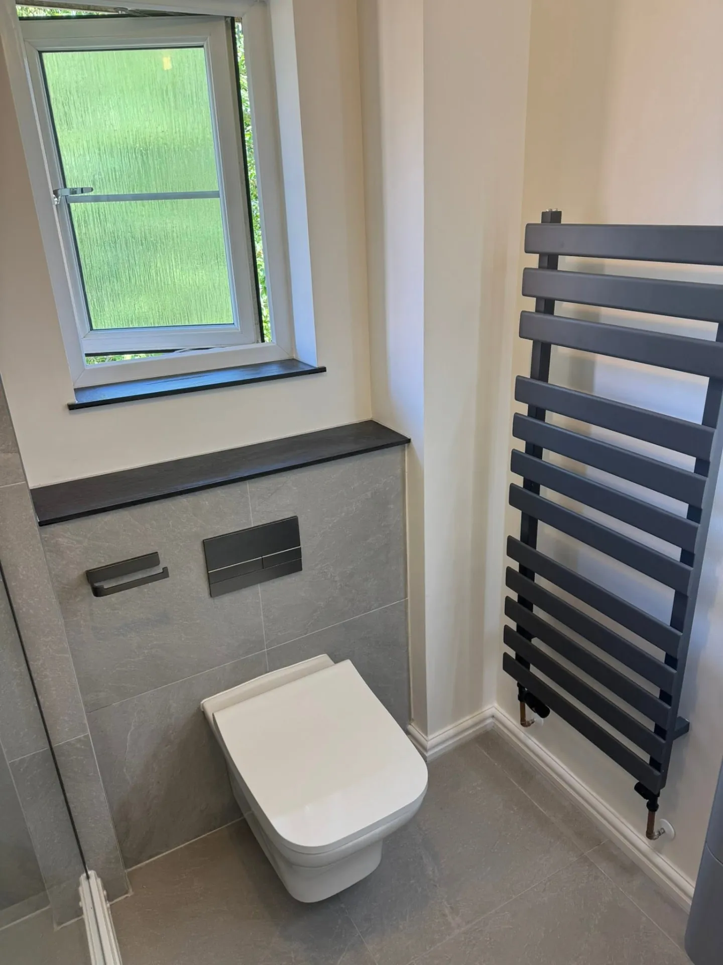Bathroom installation by Space B Tiling: toilet and towel radiator beside a window
