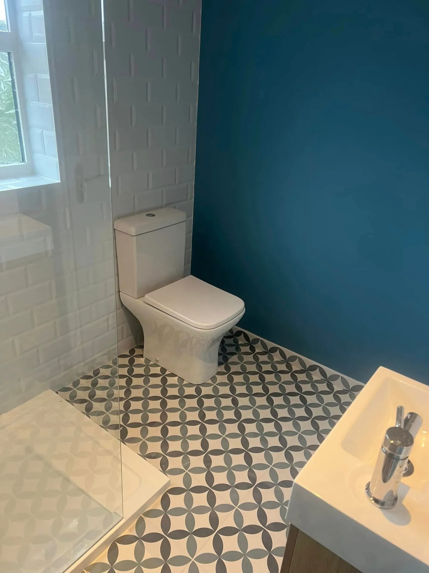 Bathroom installation by Space B Tiling: teal feature wall with white tiles and patterned floor