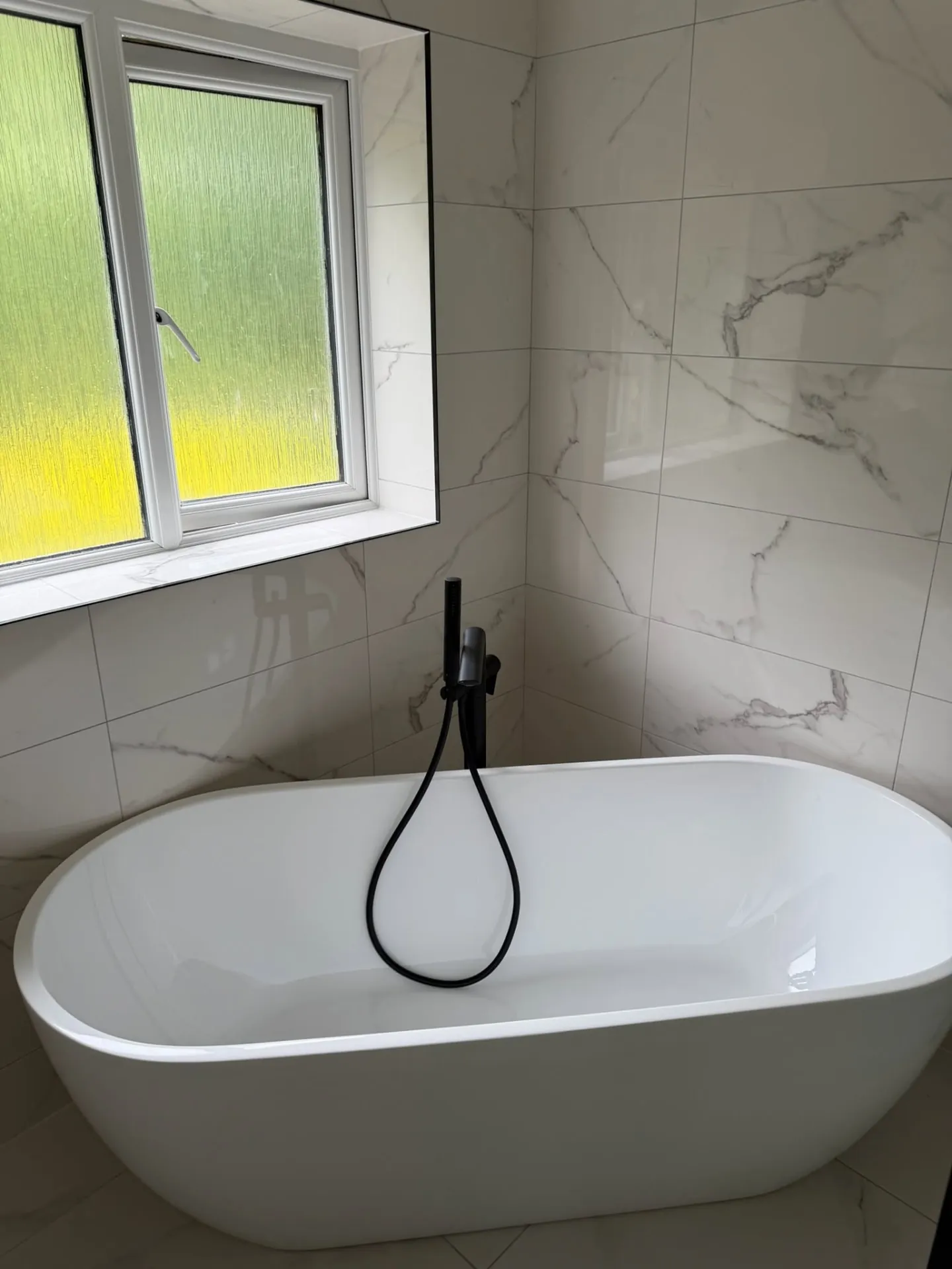 Bathroom installation by Space B Tiling: freestanding bath with black floor-standing tap and marble-effect tiles