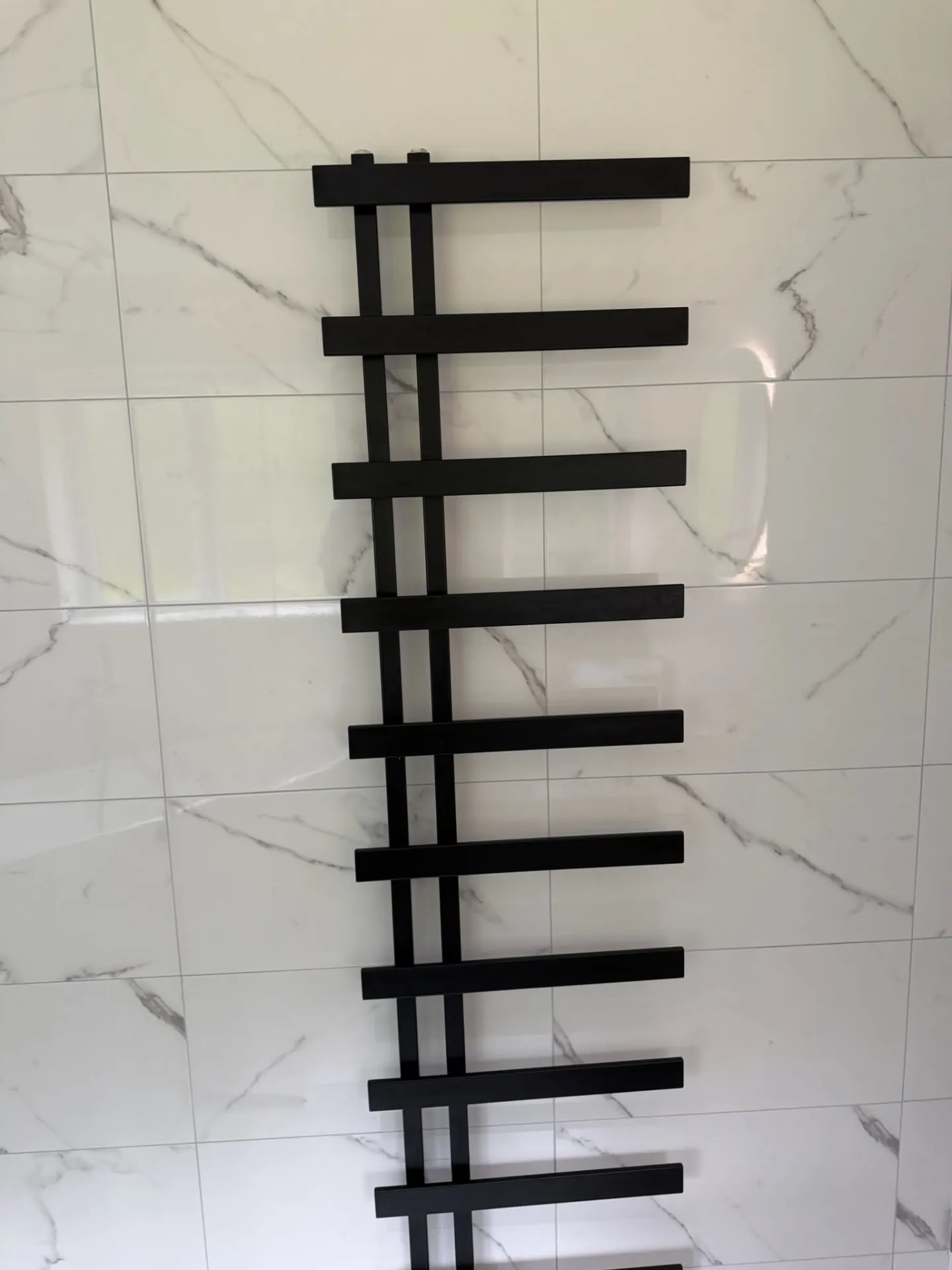 Bathroom installation by Space B Tiling: black towel radiator on marble-effect tiles