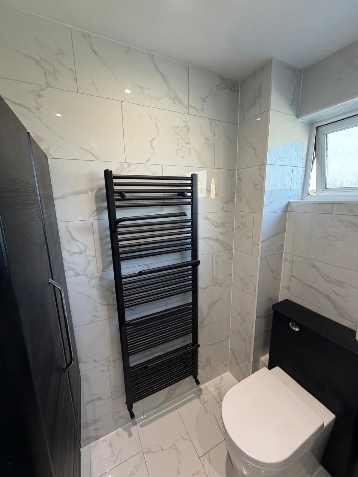 Bathroom installation by Space B Tiling: black towel radiator with marble-effect tiles