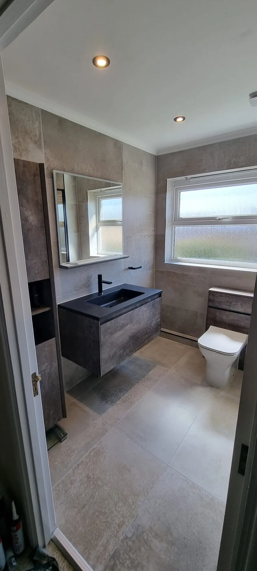 Bathroom installation by Space B Tiling: dark vanity with neutral stone-look finishes