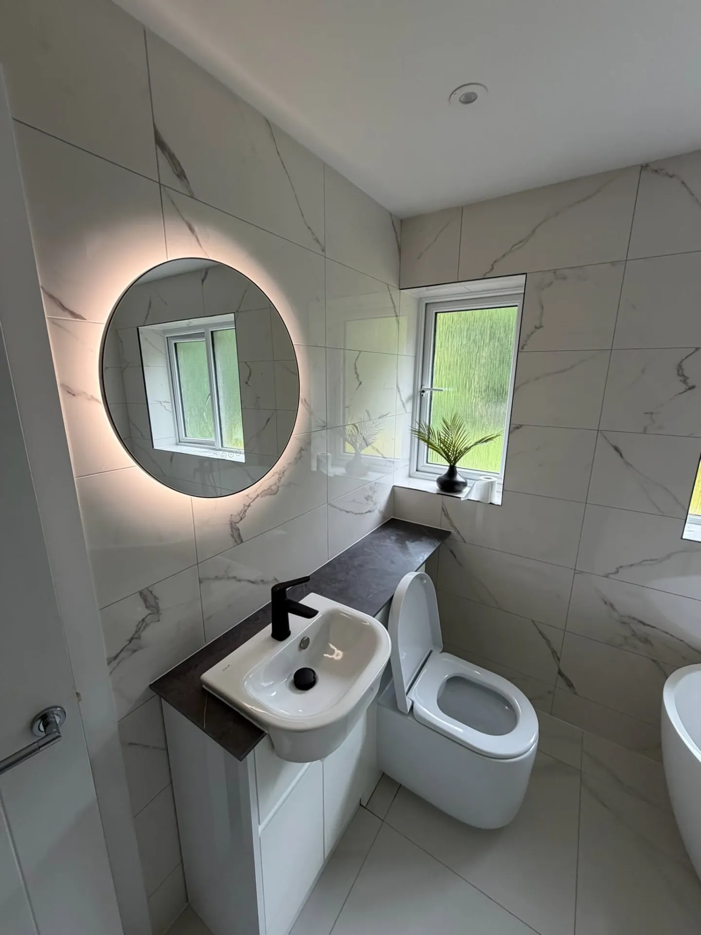 Bathroom installation by Space B Tiling: backlit round mirror, basin unit and marble-effect tiles