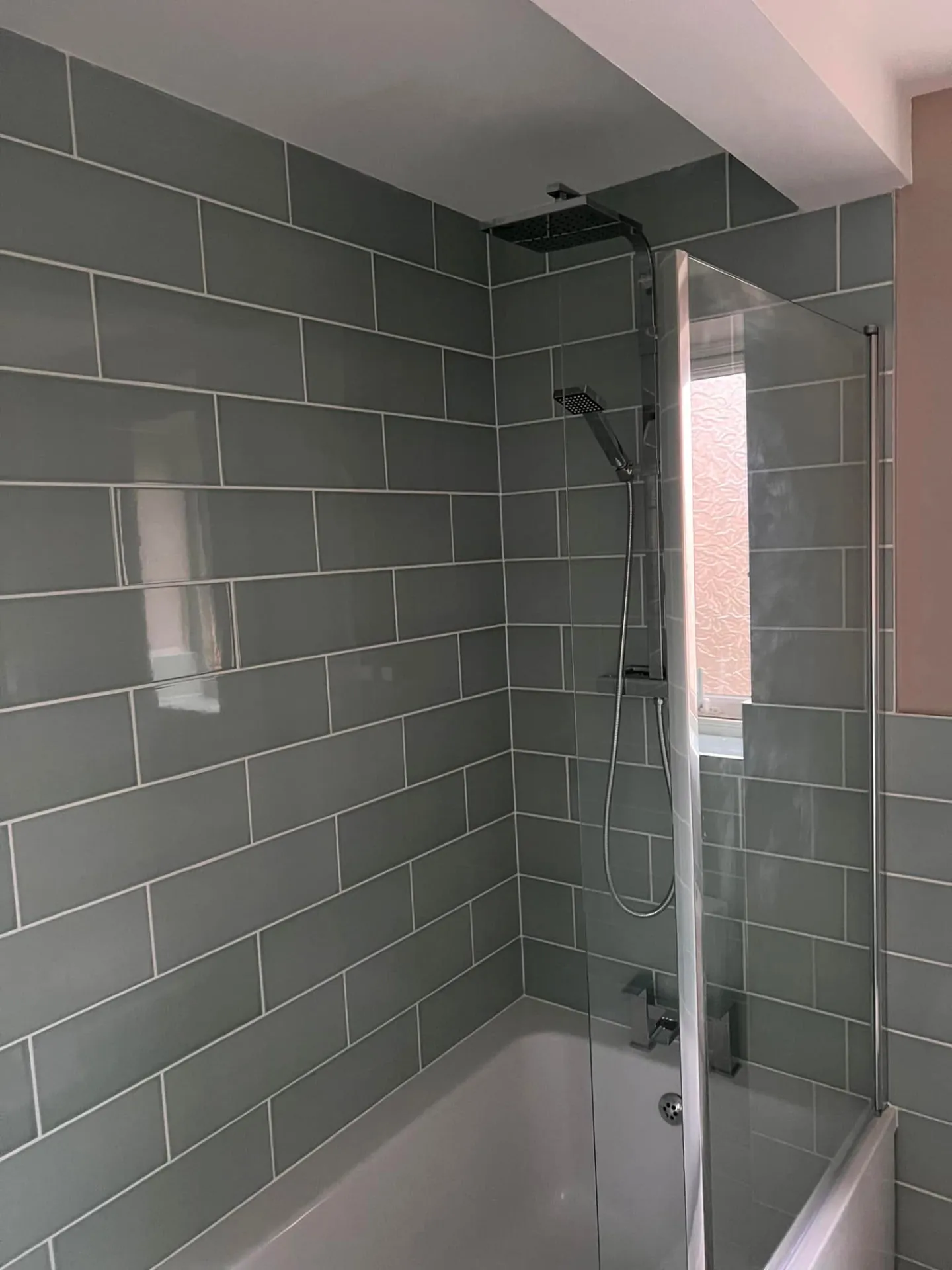 Bathroom installation by Space B Tiling: grey-tiled shower over bath with black-framed screen