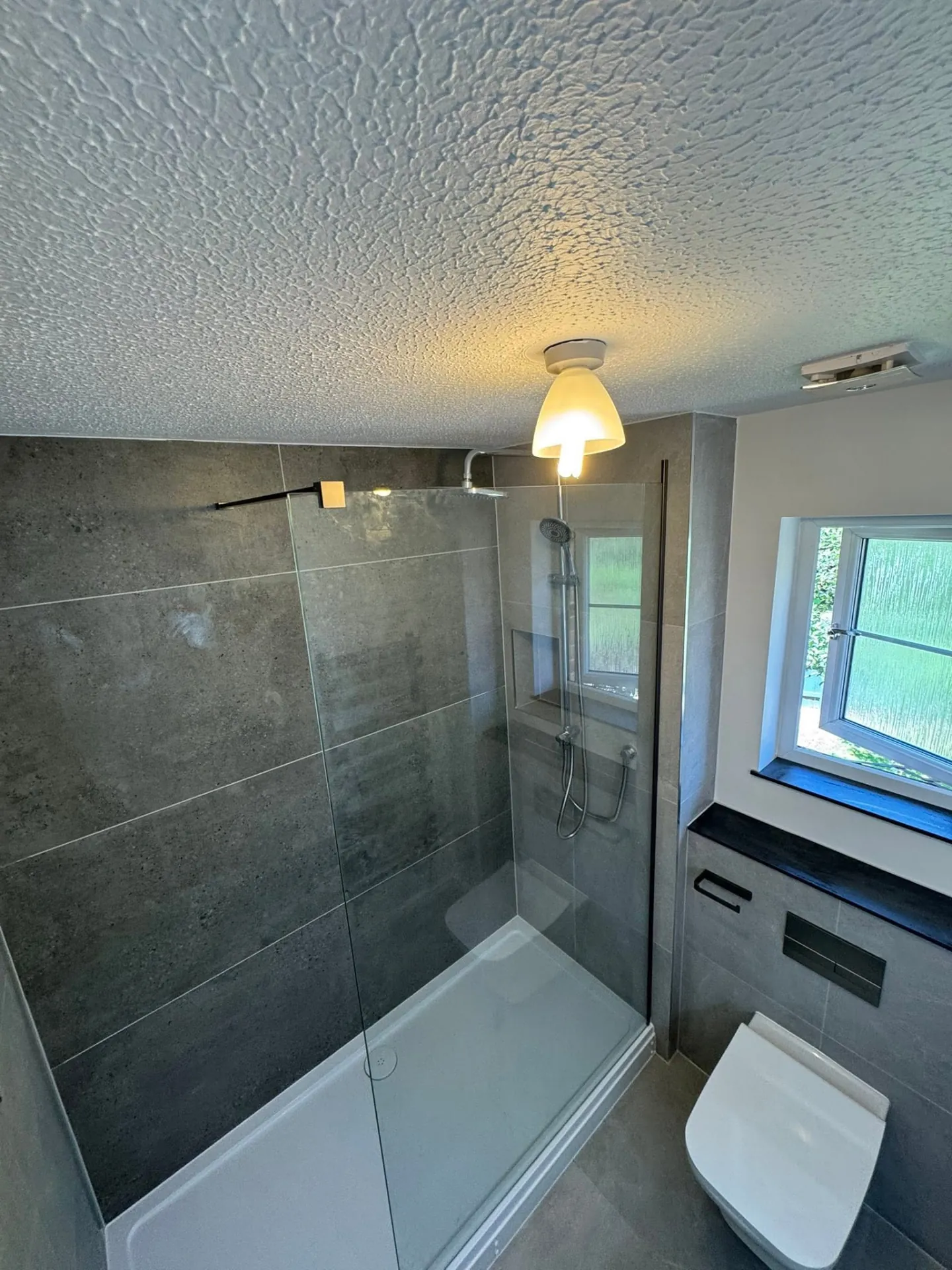 Bathroom installation by Space B Tiling: shower over bath with clear screen and dark grey tiles