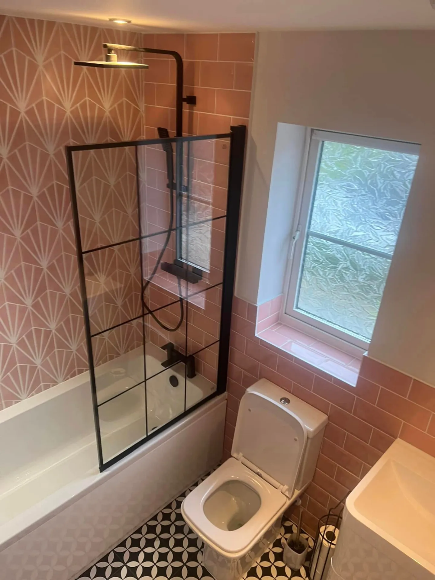 Bathroom installation by Space B Tiling: pink-tiled shower over bath with black-framed screen