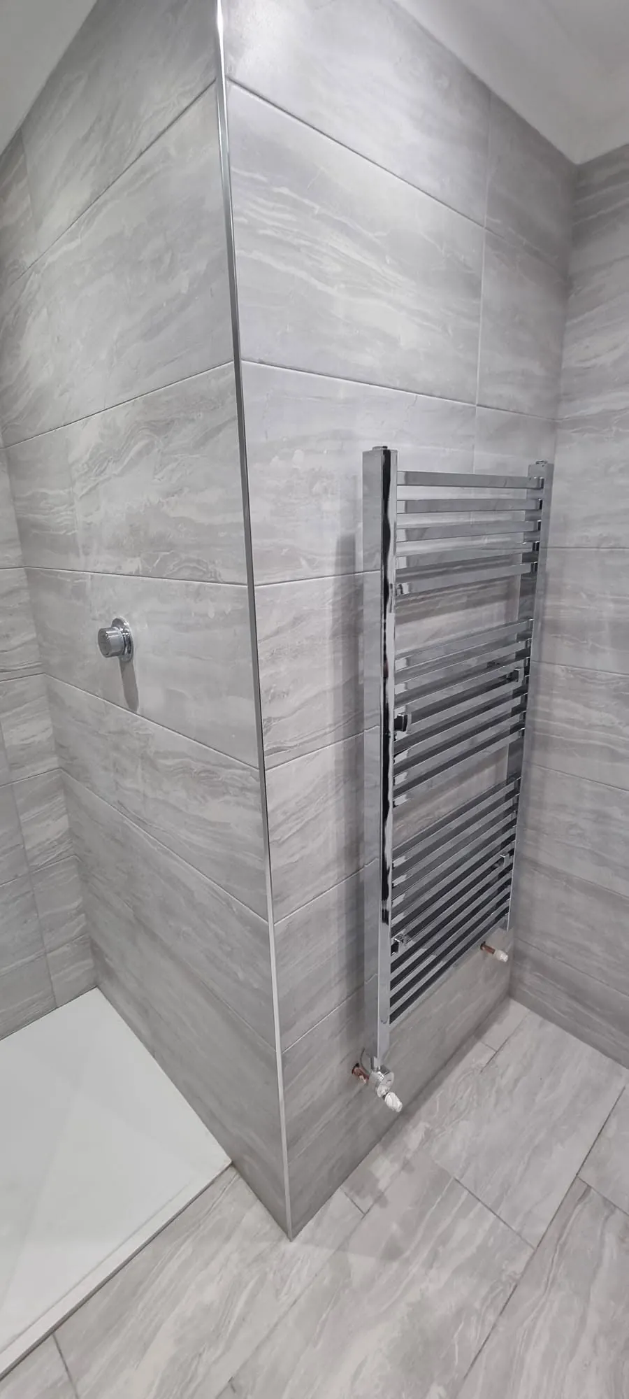 Bathroom installation by Space B Tiling: chrome towel radiator on marble-effect tiles