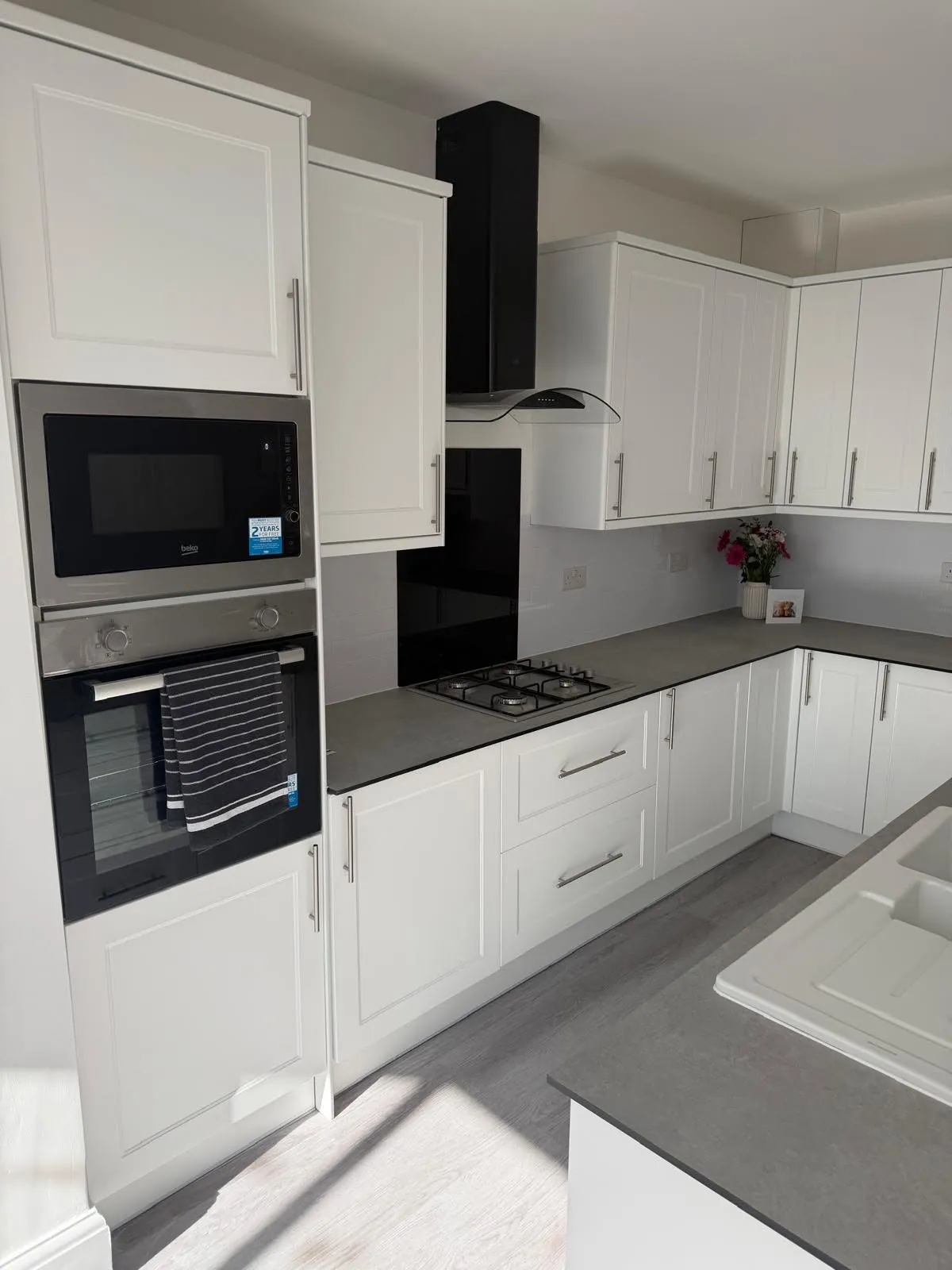 Kitchen installation by Space B Tiling: white shaker units with built-in oven and grey worktops