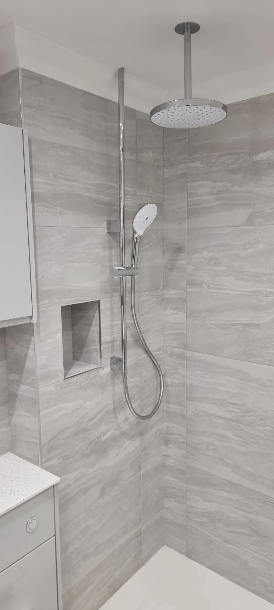 Bathroom installation by Space B Tiling: ceiling-fed rain shower with grey stone-effect tiles and niche