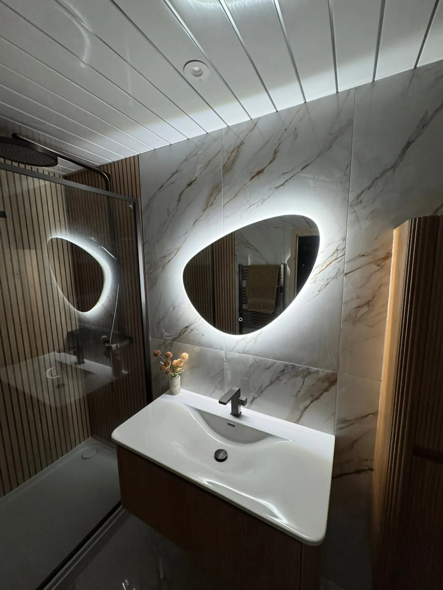 Bathroom installation by Space B Tiling: backlit mirror, marble-effect tiles and fluted wall panels
